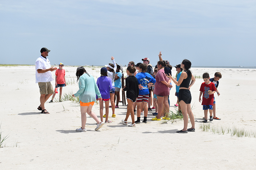 Students hold up their hands to observe the wind on a beach.