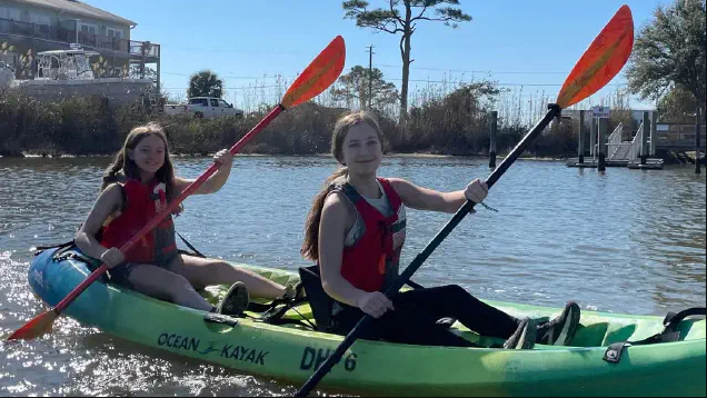 Two students paddling on the water in a green kayak